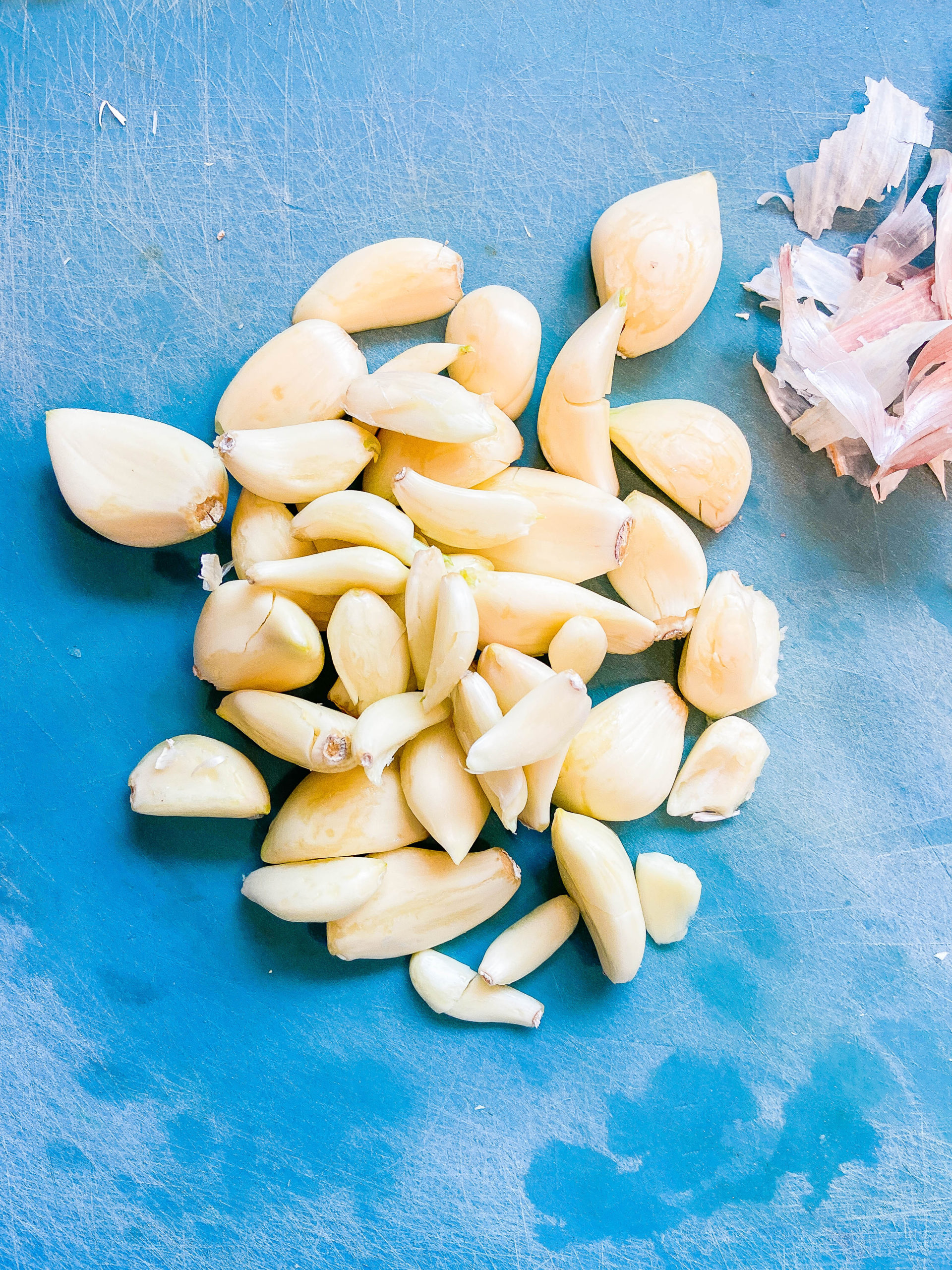 Peeled garlic cloves on a blue cutting board. 