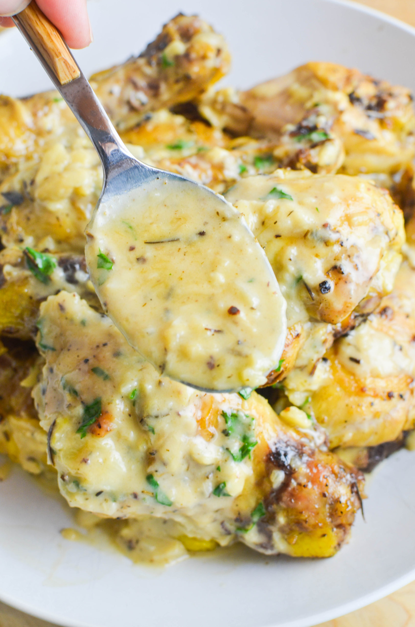 Une cuillère de sauce à l'ail avec le poulet en arrière-plan.