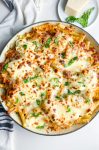 Overhead photo of baked ziti in a skillet with a stripped towel and parmesan cheese.