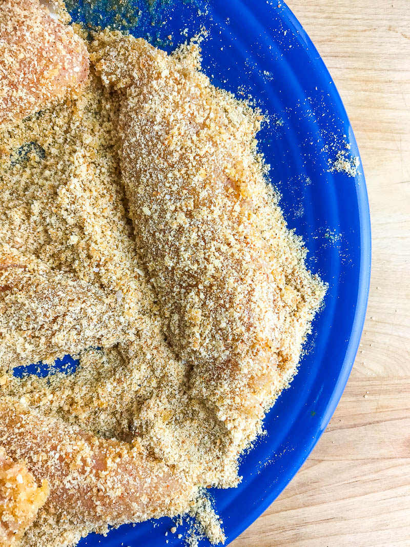 Chicken tenderloins coated in seasoned bread crumbs in a plate. 