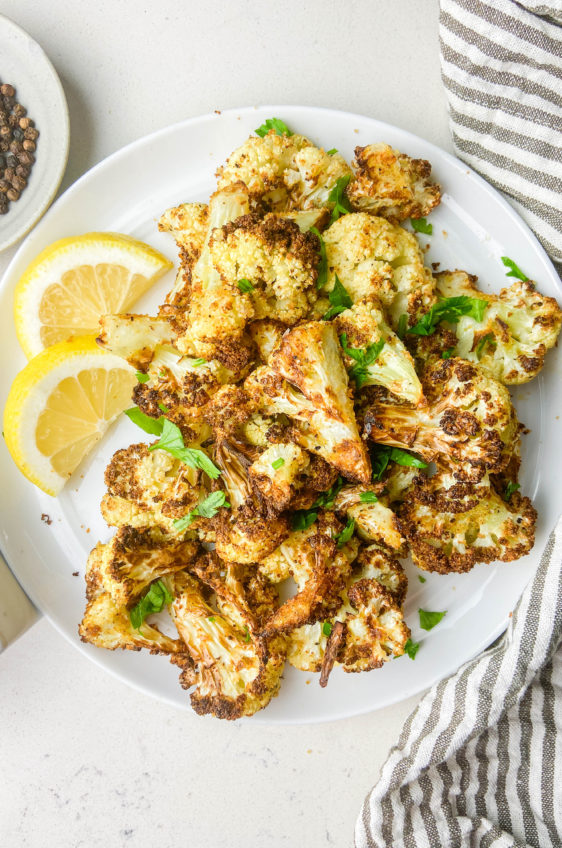 Overhead photo of cauliflower on white plate with lemons and stripped napkin.