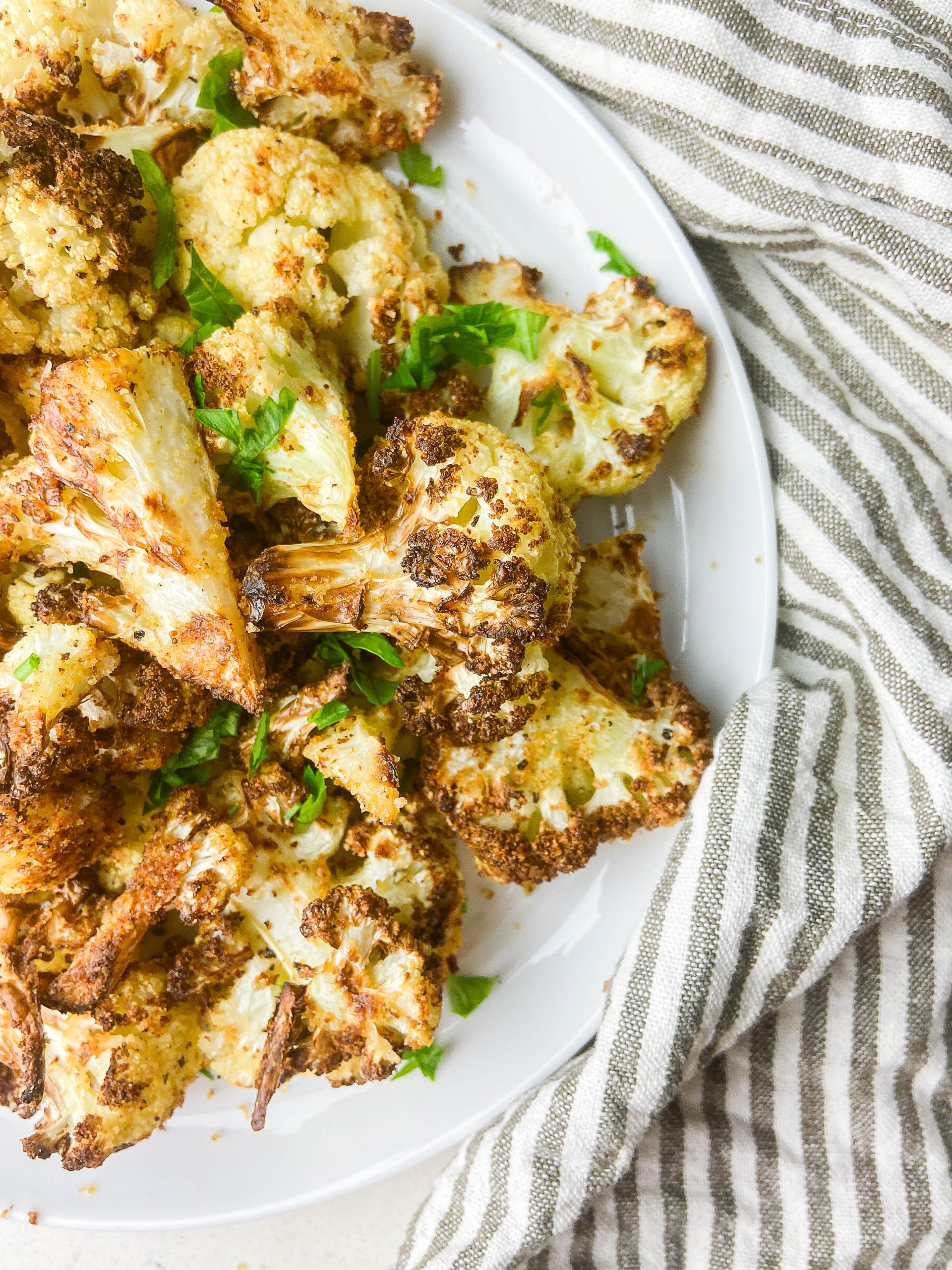 Overhead photo air fryer cauliflower on a white plate with a striped napkin. 