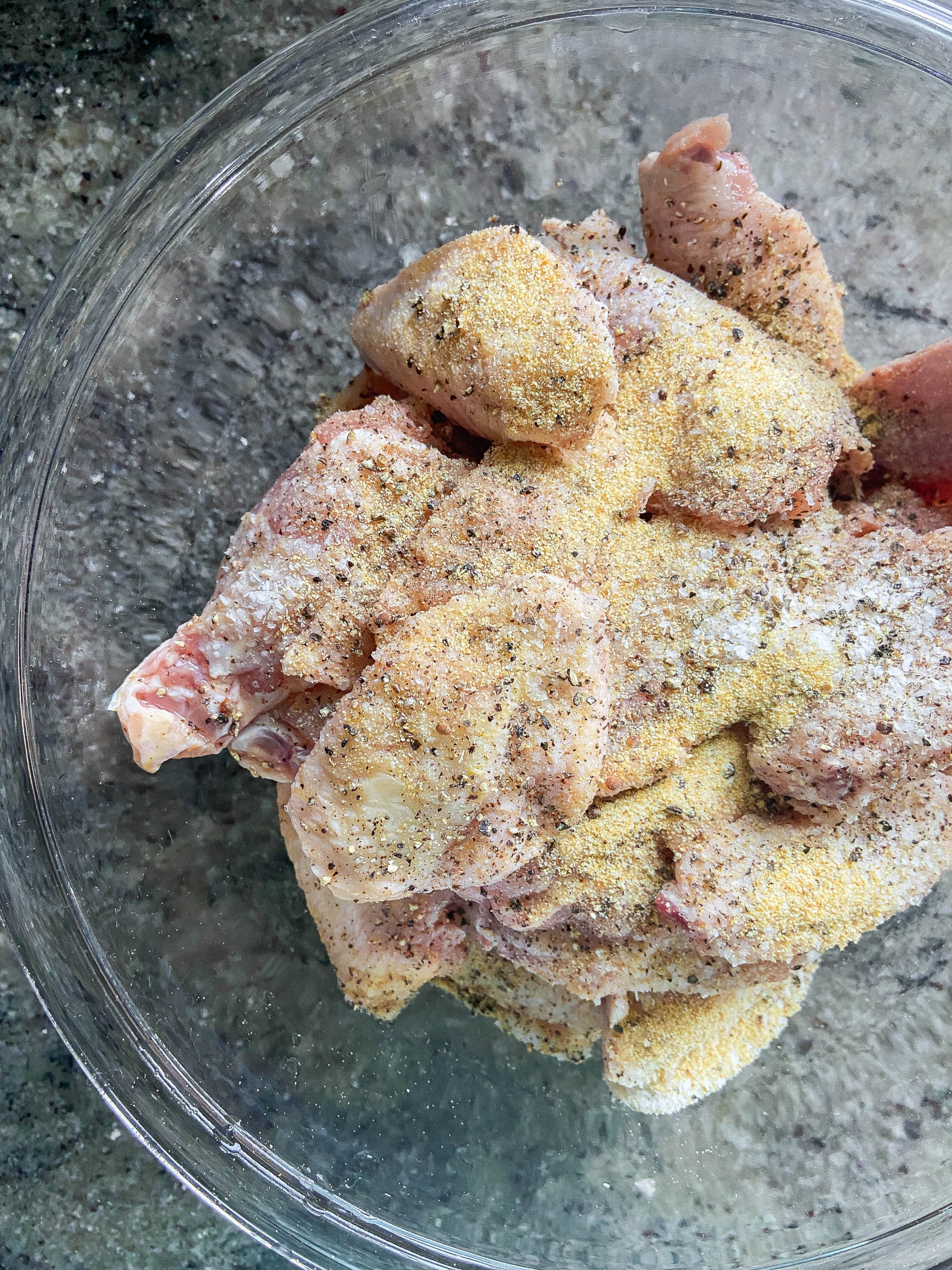 Raw chicken wings in glass bowls with seasonings. 