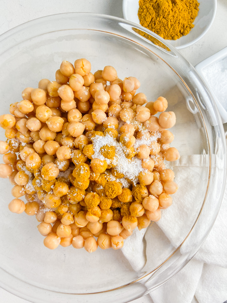 Chickpeas with salt, curry powder and oil in a glass bowl. 