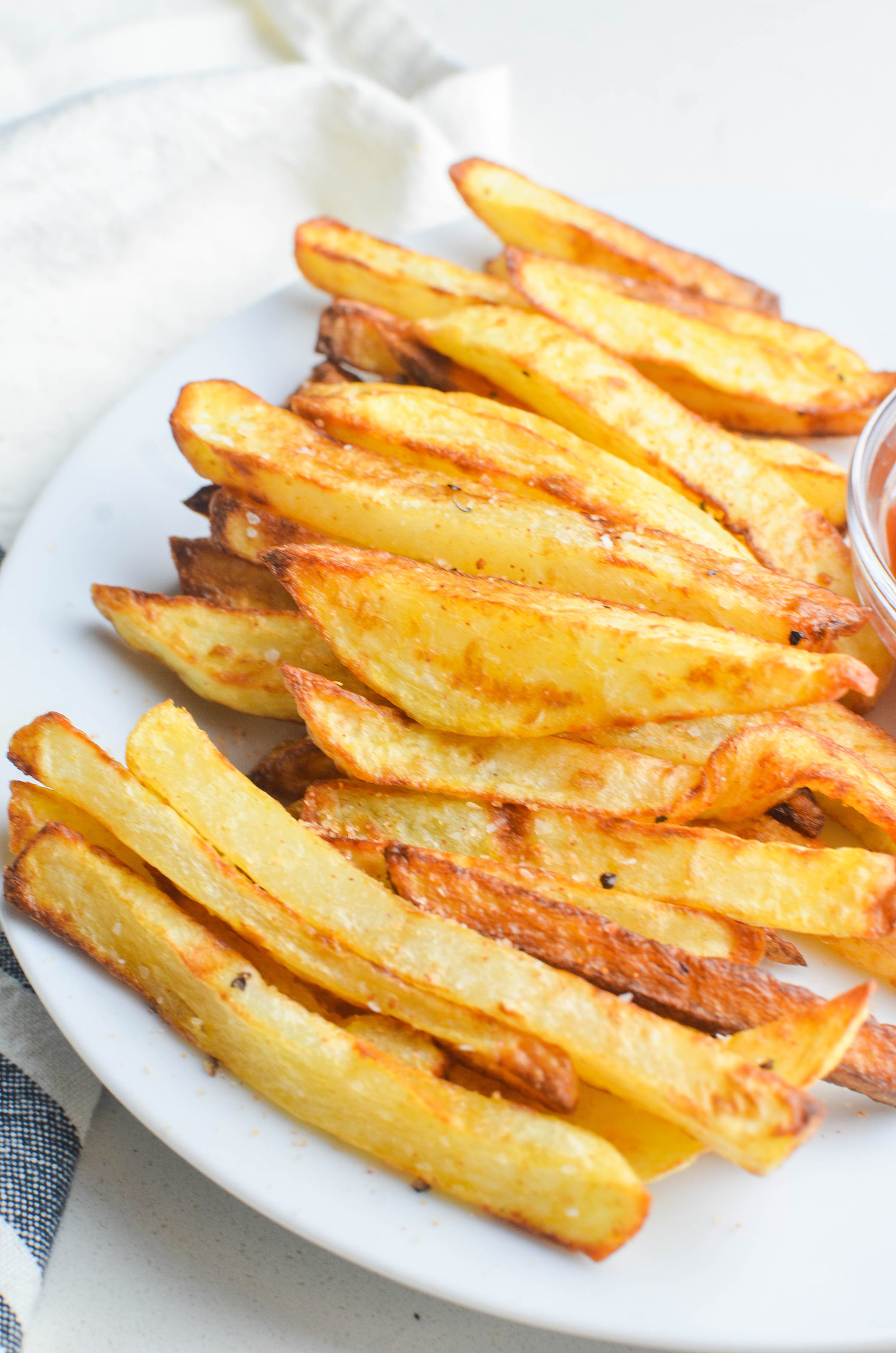 Side angle photo of air fried french fries on a white plate. 