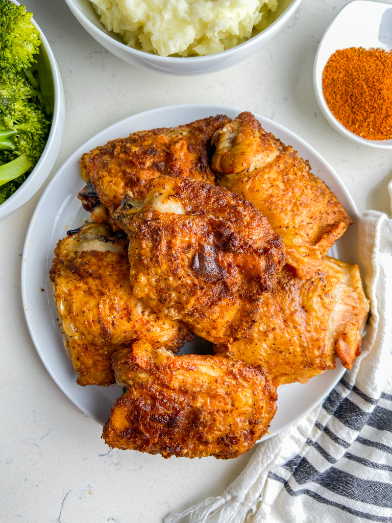 Overhead photo of air fryer chicken thighs on white plate with broccoli and mashed potatoes. 