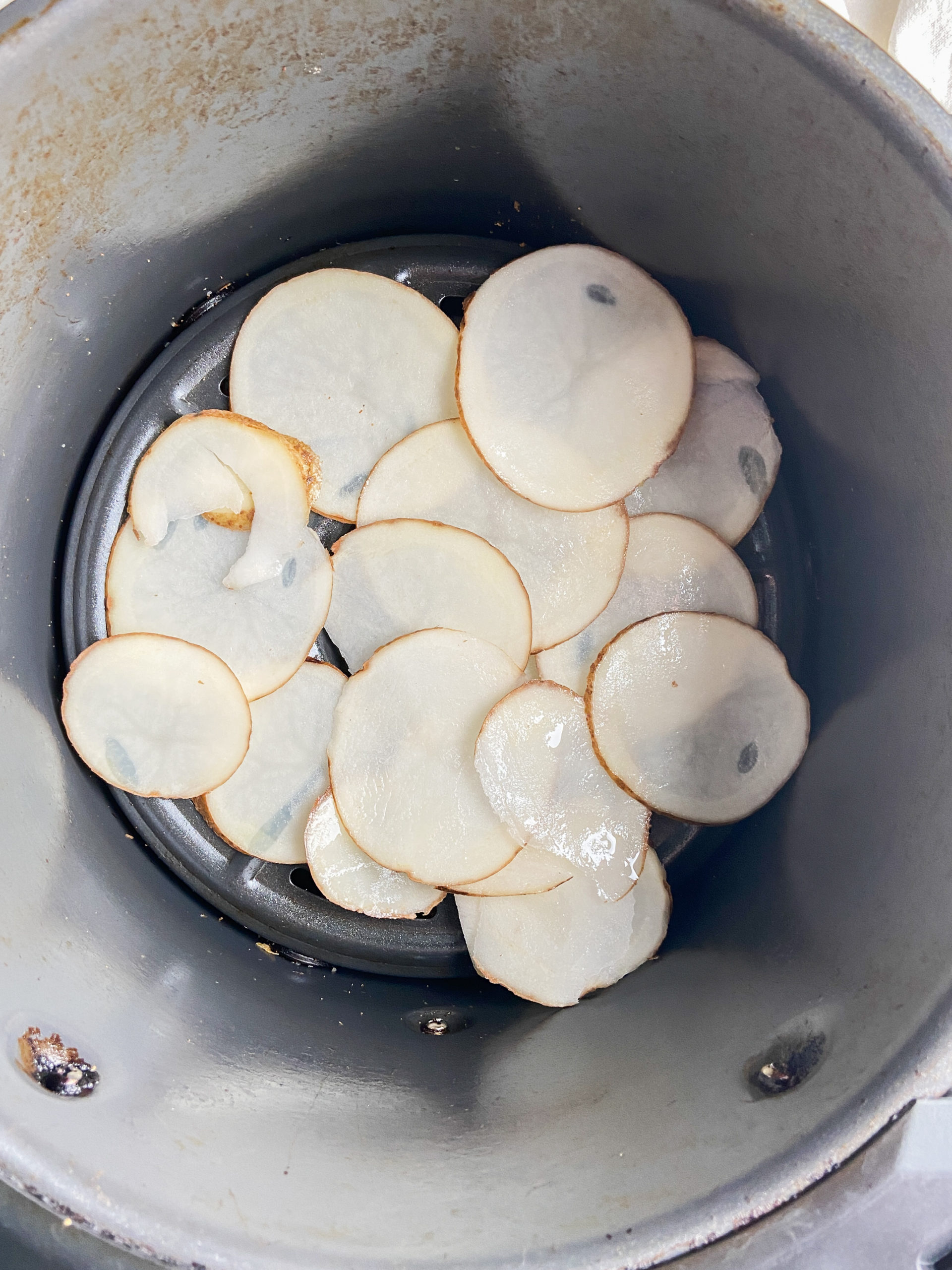 Potato slices in air fryer basket. 