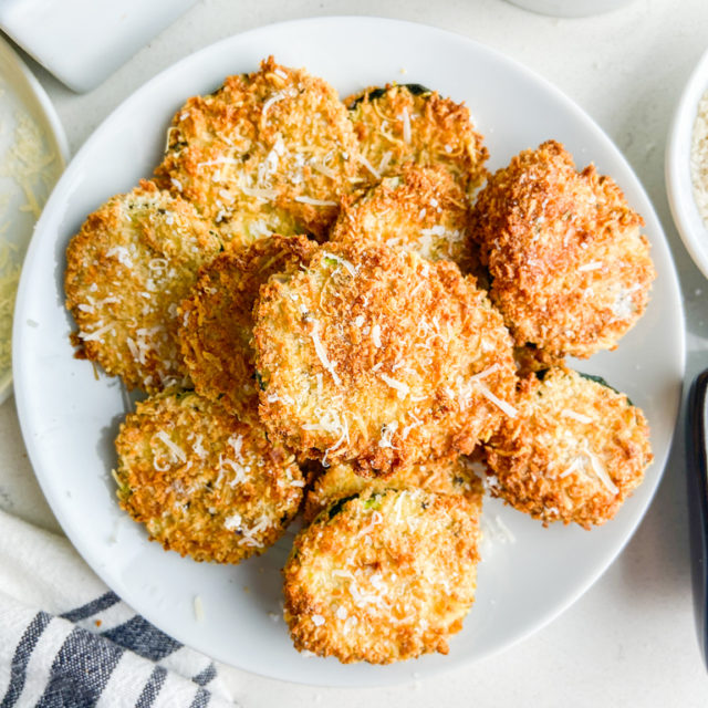 Overhead photo of crispy zucchini chips on white plate.