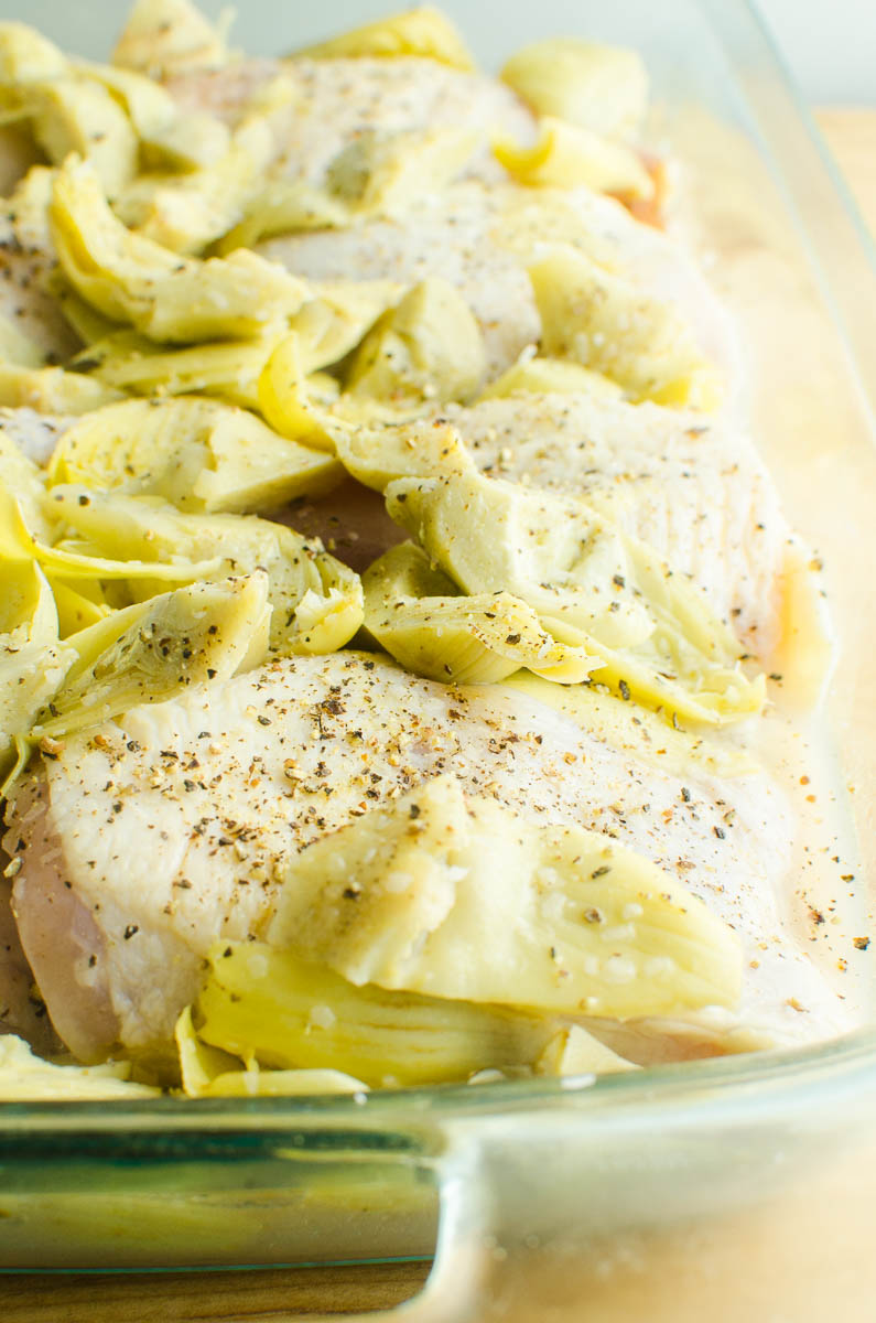 Raw chicken thighs with salt, pepper and artichoke hearts. 