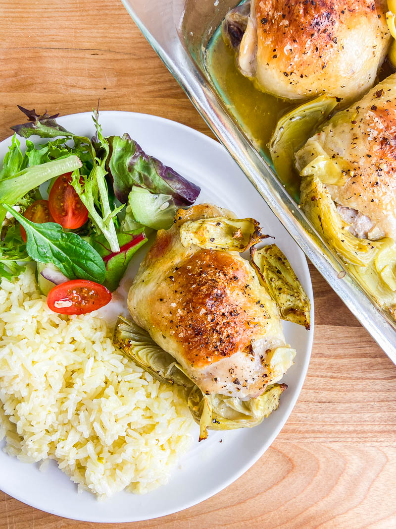 Artichoke Chicken on a white plate with salad and rice. 