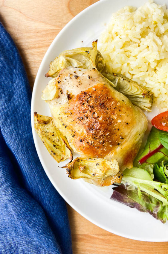 Artichoke Chicken on a white plate with salad and rice. Blue napkin on side.