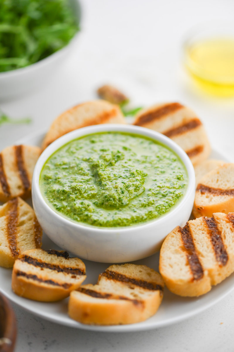 Arugula pesto in a white bowl with grilled toasts. 