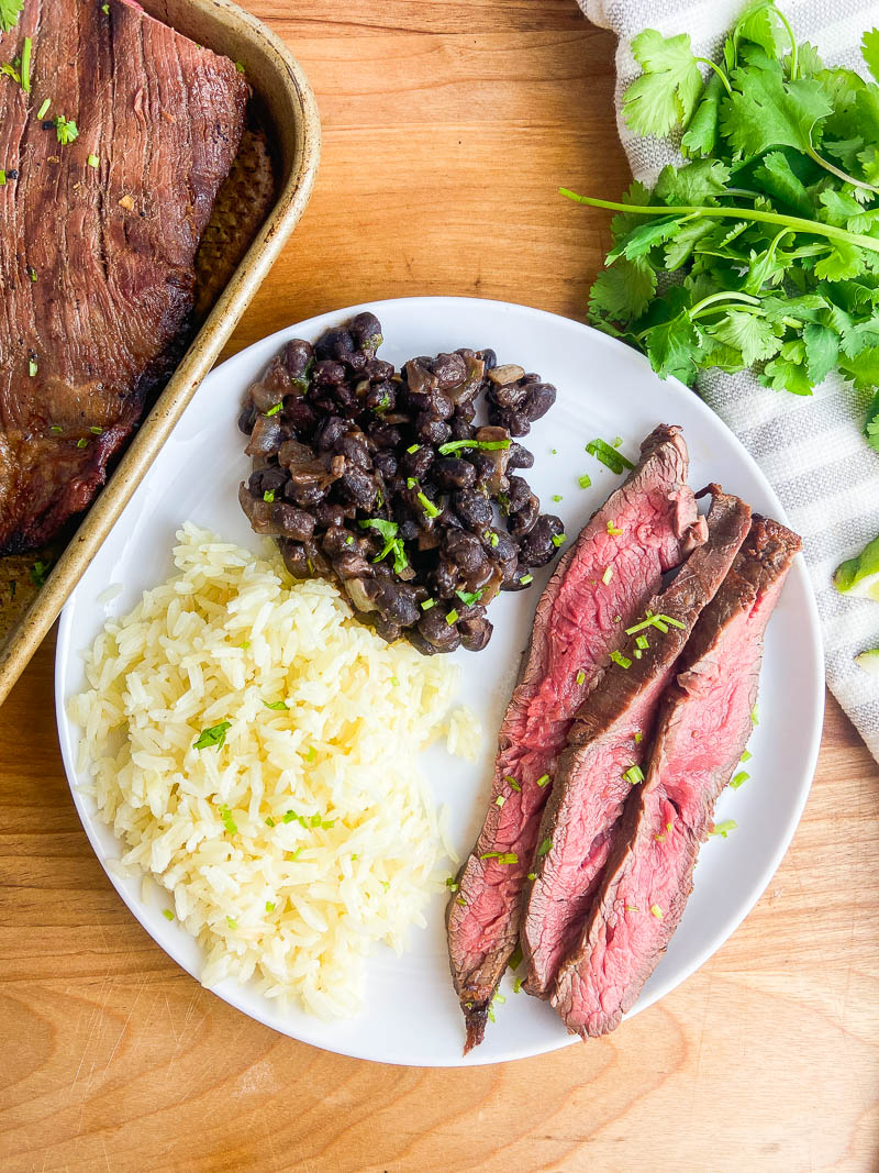 Overhead photo of sliced carne asada on a white plate with beans and rice.