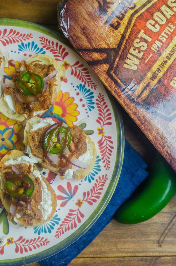 BBQ Pulled Pork Bruschetta is topped with goat cheese, Curly’s RoadTrip Eats West Coast IPA Style Pulled Pork, onions, jalapenos and BBQ sauce. It’s perfect for game day!