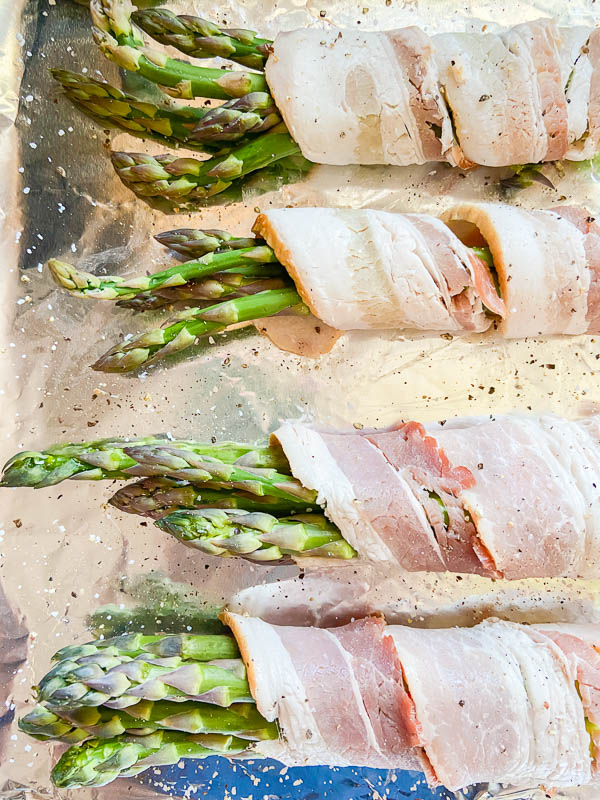 Bacon wrapped asparagus sprinkled with salt and pepper on an aluminum foil lined baking sheet. 