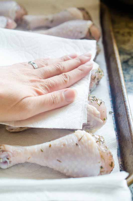 Patting dry brined chicken with a paper towel. 
