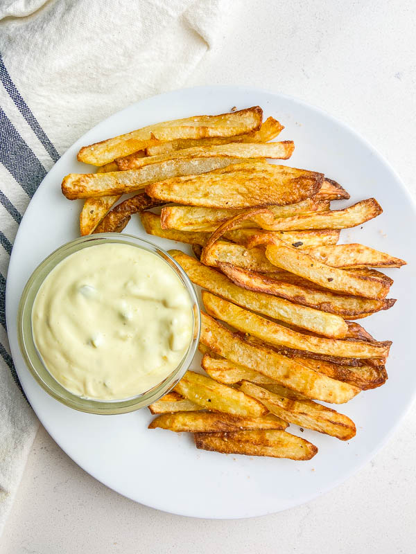 Overhead photo of french fry dip and fries on a white plate with striped towel. 