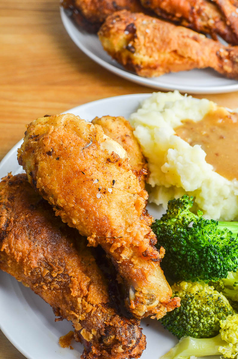 Buttermilk fried chicken on a white plate with mashed potatoes, gravy and broccoli. 