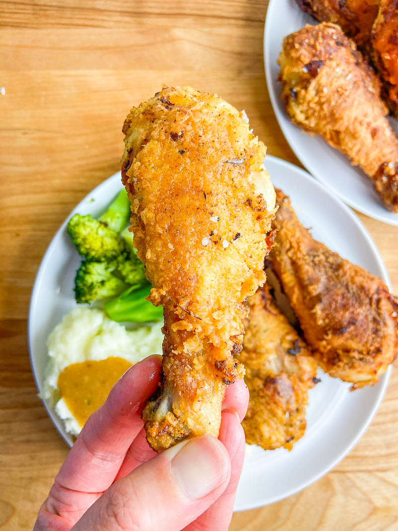 A hand holding a piece of buttermilk fried chicken 