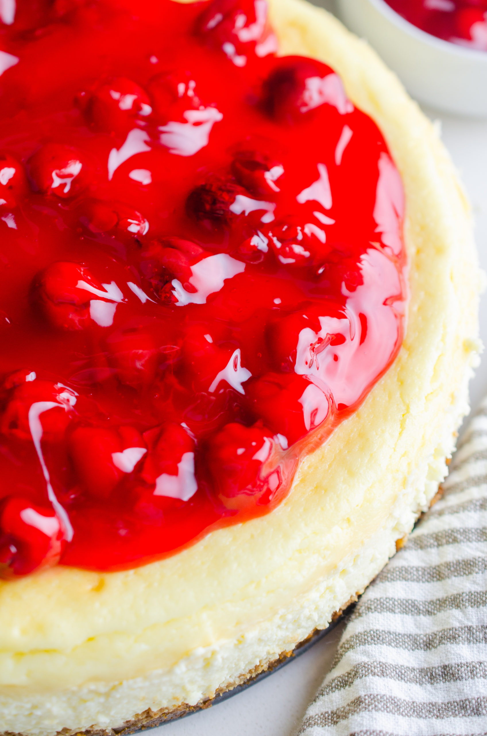 Side photo of cheesecake with cherry pie filling spooned on top. 