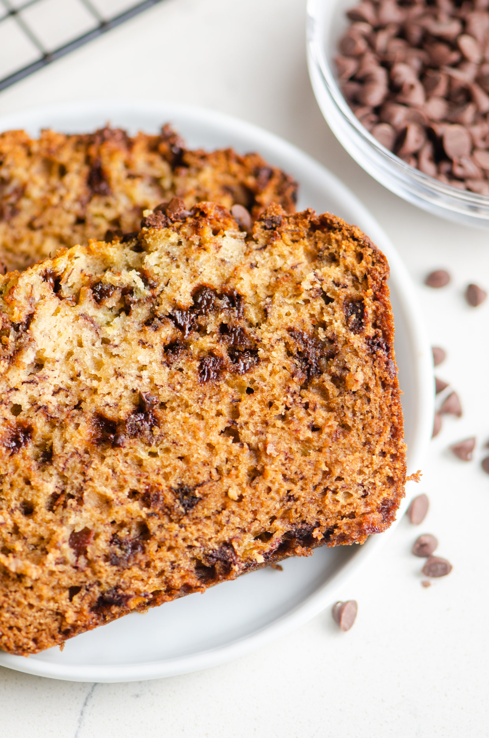 Two slices of banana bread on a white plate with chocolate chips next to it 