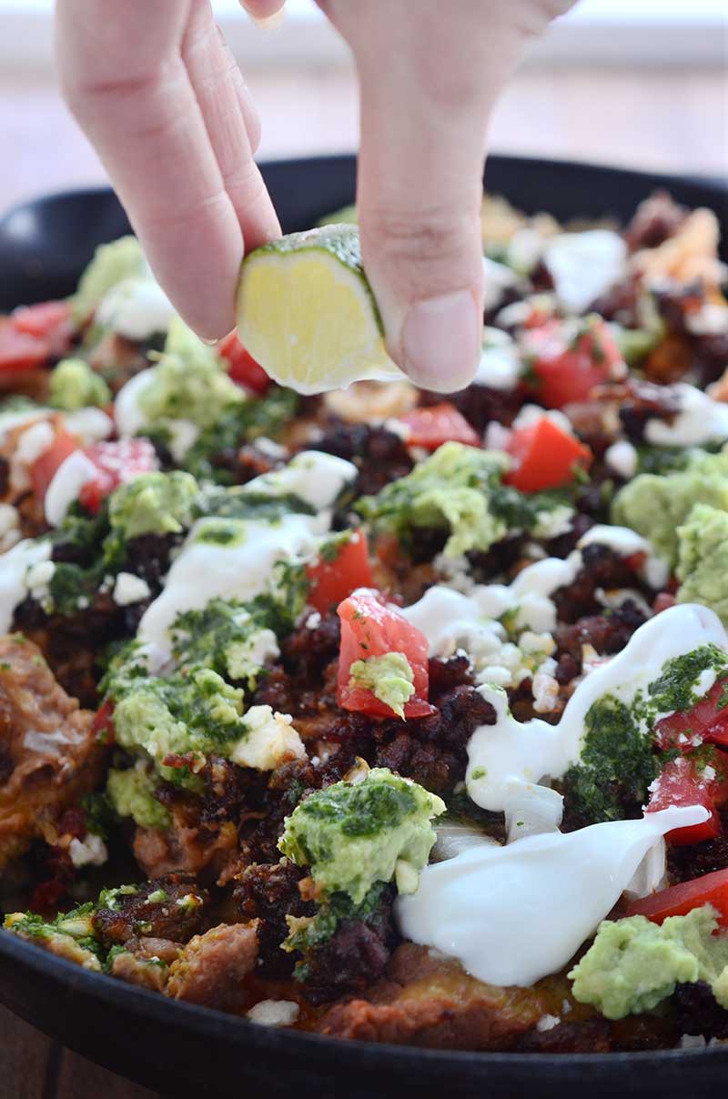 Chorizo Skillet Nachos are fully loaded with chips, refried beans, cheese, chorizo, guacamole, sour cream, onions, tomatoes and Habanero Chimichurri.