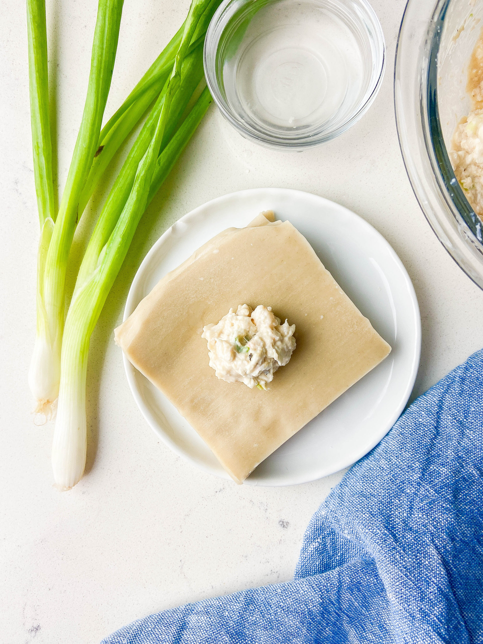 filling in the center of a wonton wrapper with green onions, blue napkin and bowl of water. 