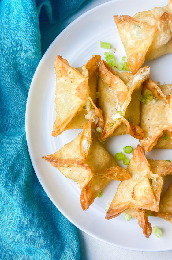 Overhead photo of crab rangoon on a white plate with a teal napkin.