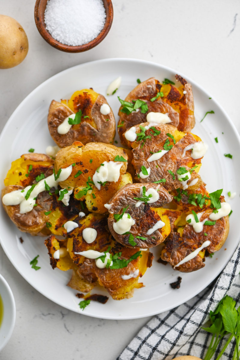 Crispy Smashed Potatoes drizzled with truffle aioli on white plate.