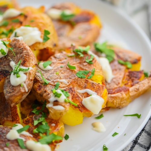 Smashed Potatoes drizzled with aioli on white plate.