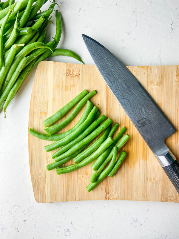 Green beans on a wooden cutting board with a knife. 