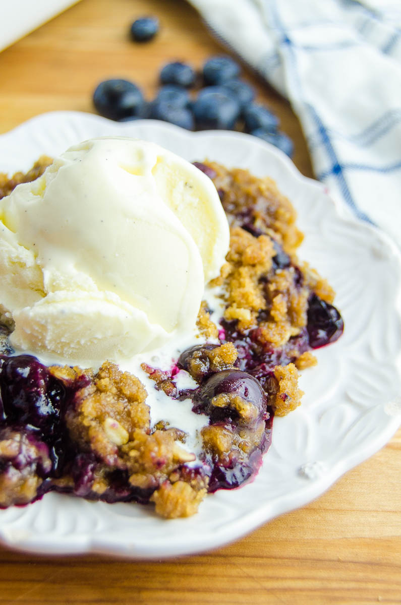 Side angle photo of blueberry crisp with ice cream on top. 
