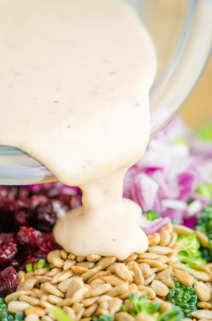 Pouring salad dressing over broccoli salad. 