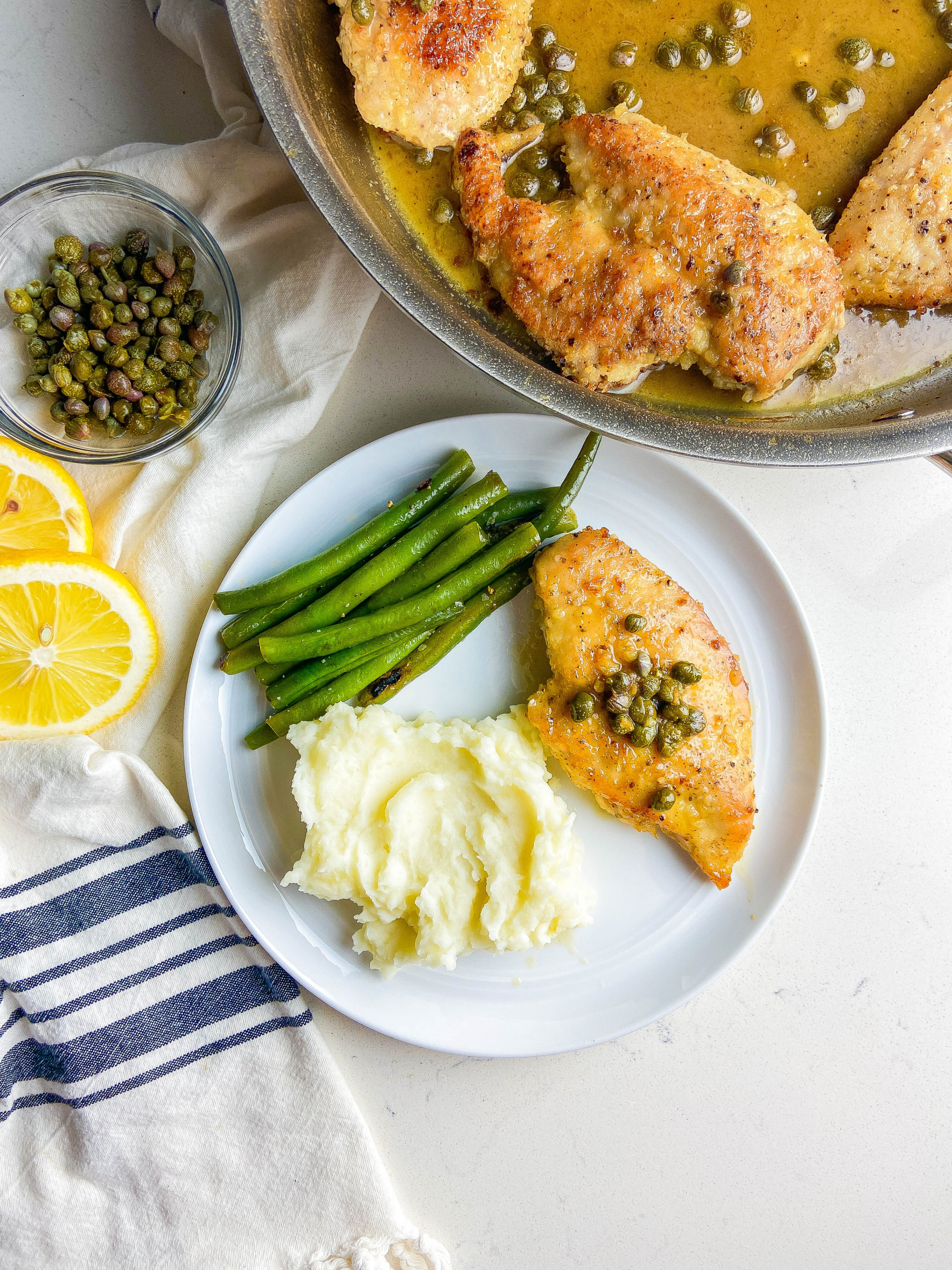 Overhead photo of chicken piccata on a plate with mashed potatoes and green beans. 