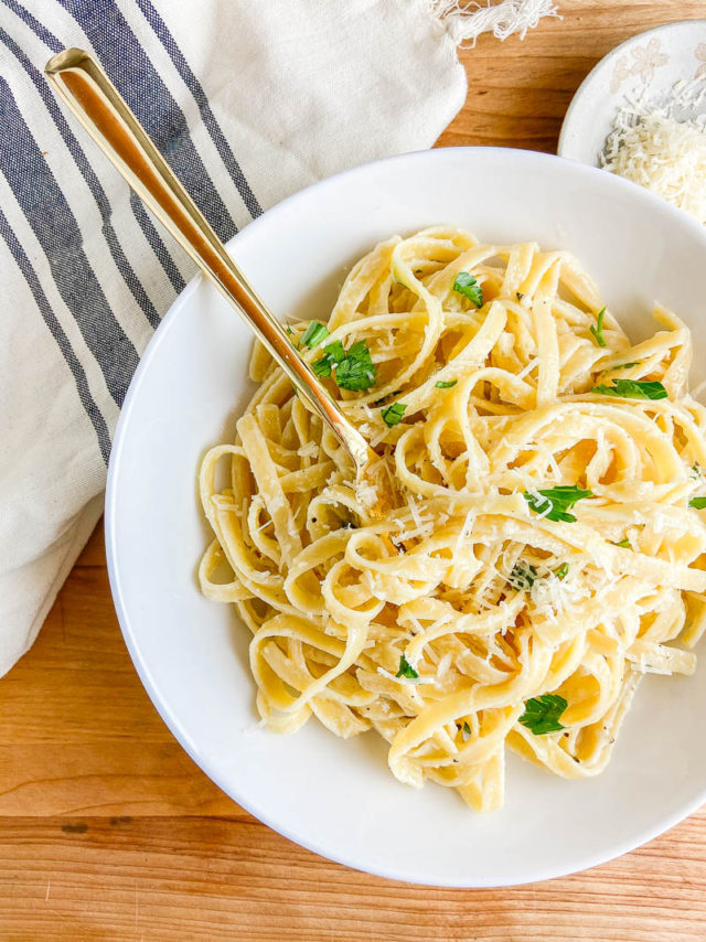 Overhead photo of fettuccine alfredo in a white bowl on wood cutting board. 