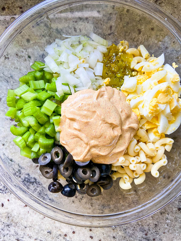 An overhead photo of all of the ingredients for macaroni salad in a glass bowl. 