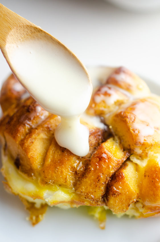 Drizzling frosting onto eggnog french toast casserole with a wooden spoon.
