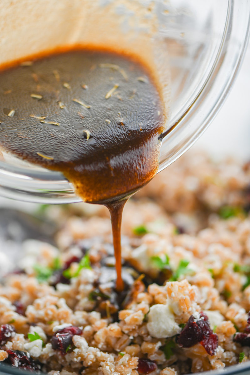 Pouring salad dressing over farro salad. 