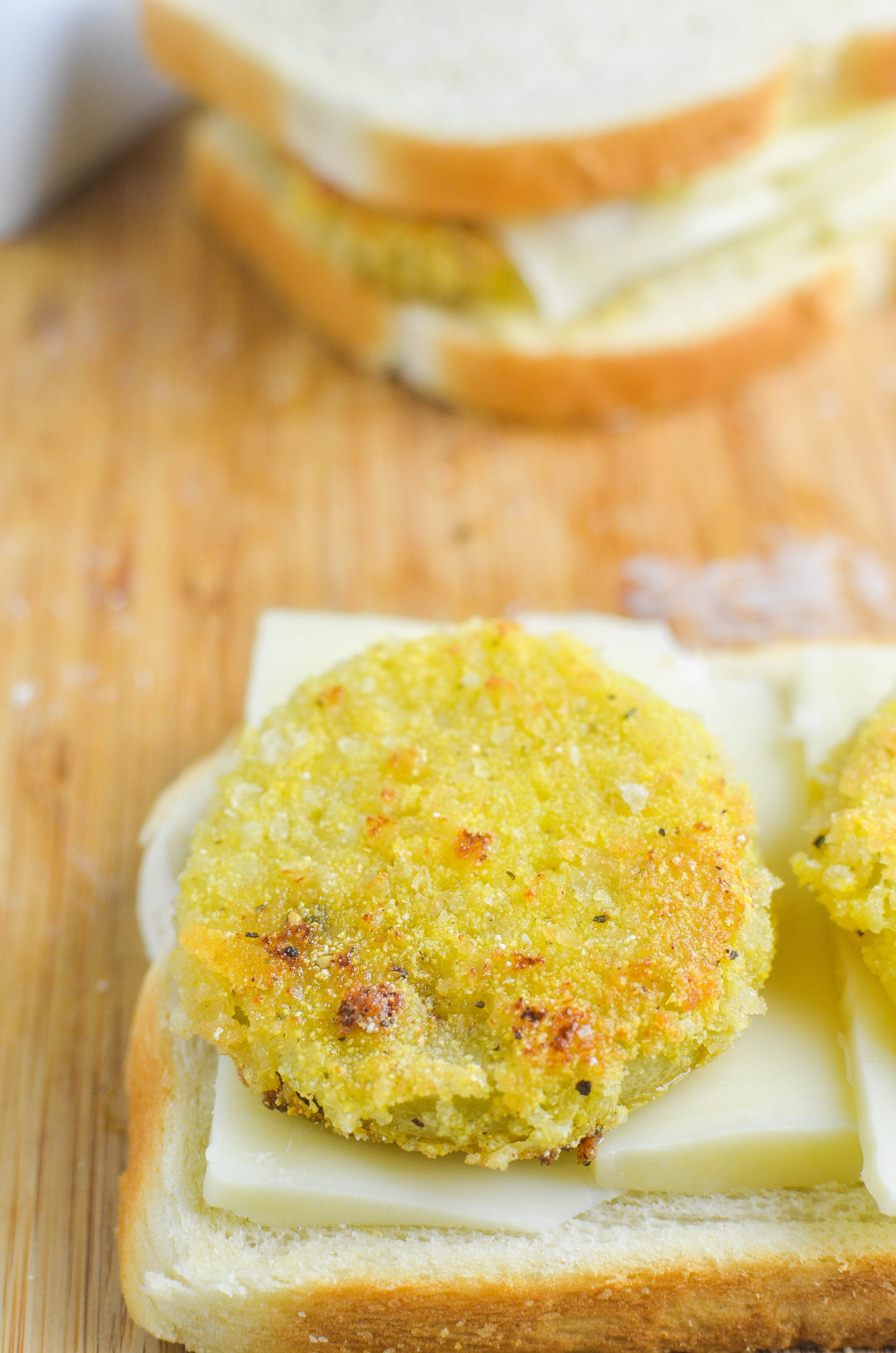 Assembling a fried green tomato grilled cheese. Two green tomatoes on top of mozzarella on bread. 