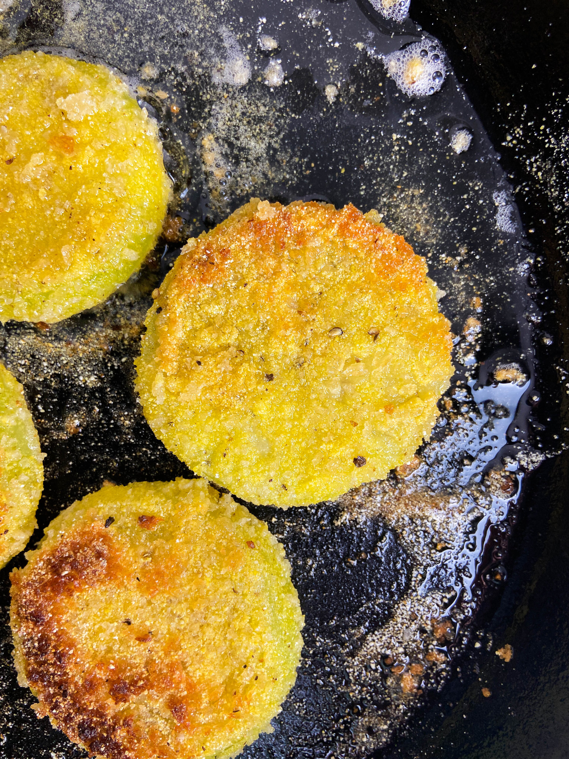 Green tomatoes frying in a cast iron skillet.