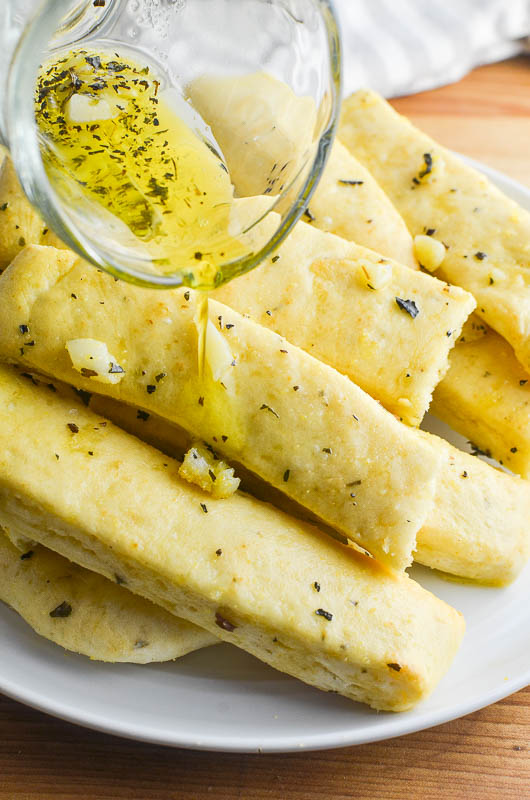 Pouring garlic butter over breadsticks. 