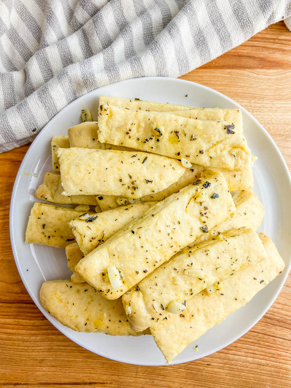 Overhead photo of garlic breadsticks on a white plate and wooden cutting board. 