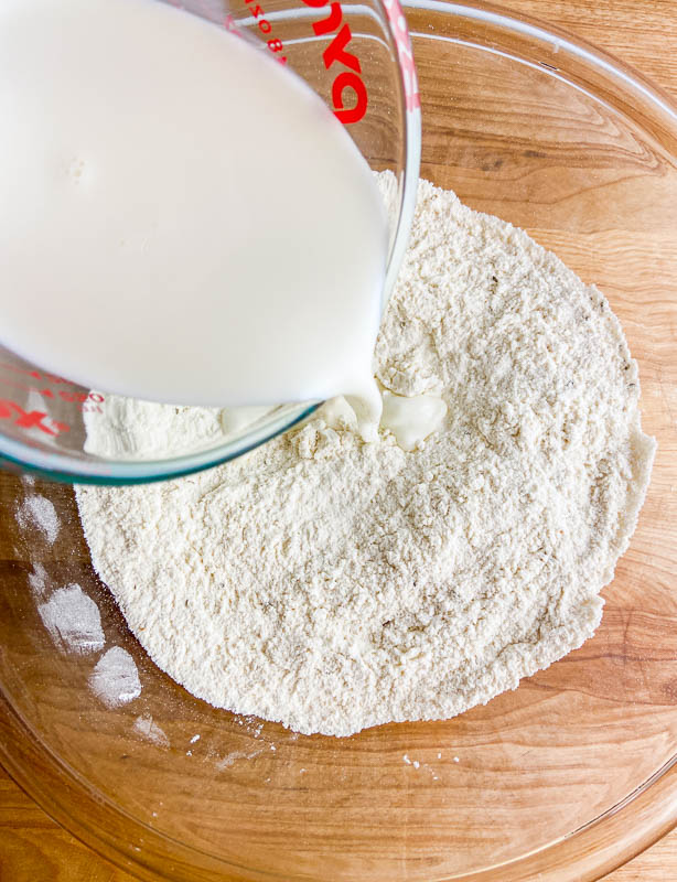 Pouring milk into dry ingredients in a clear bowl.