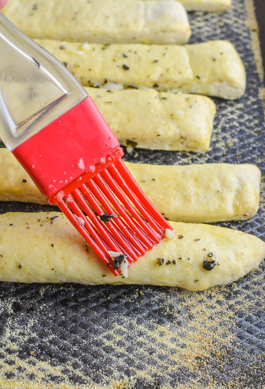 Brushing garlic butter on breadsticks with a red pastry brush. 
