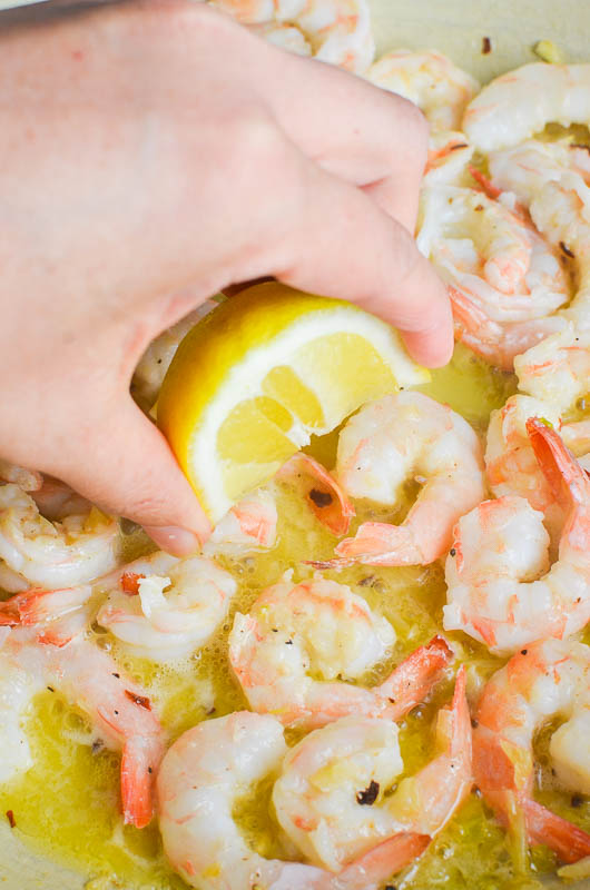 A lemon wedge squeezing lemon juice on shrimp in a pan. 