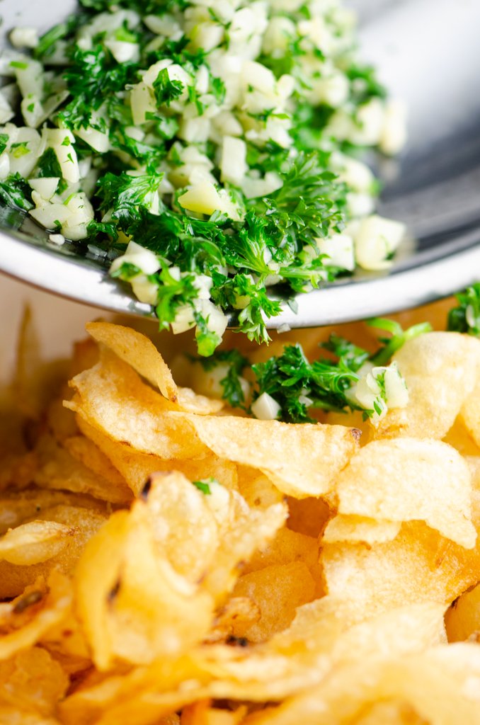 Pouring garlic and parsley over the top of chips. 