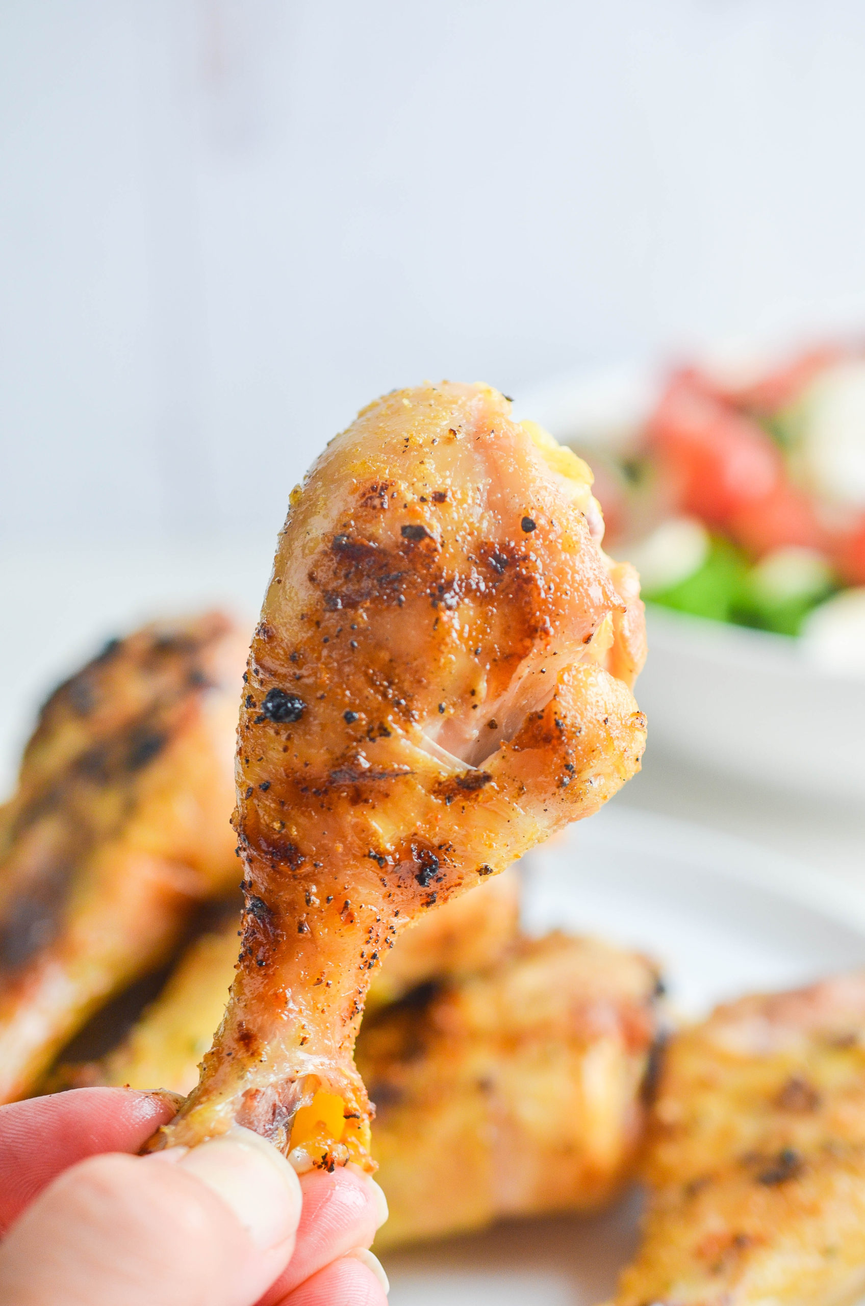 A hand holding a grilled chicken drumstick