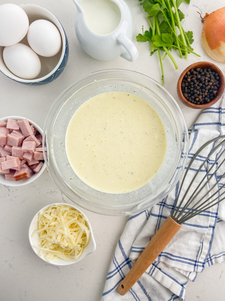 Eggs and cream whisked together in glass bowl. 