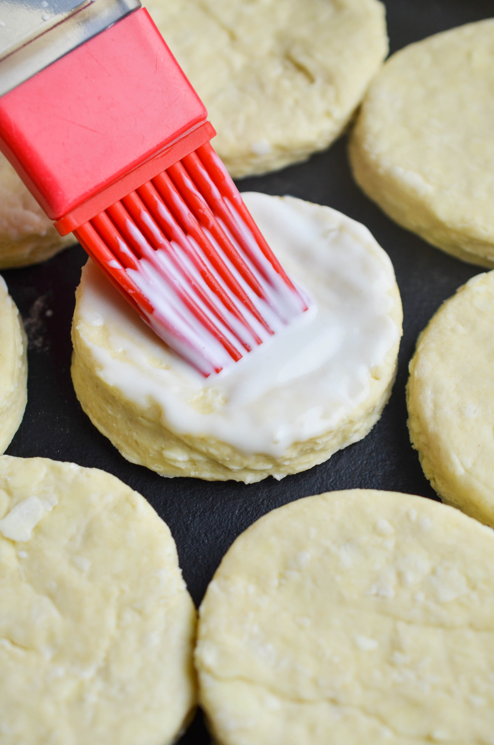Brushing buttermilk on top of biscuits. 