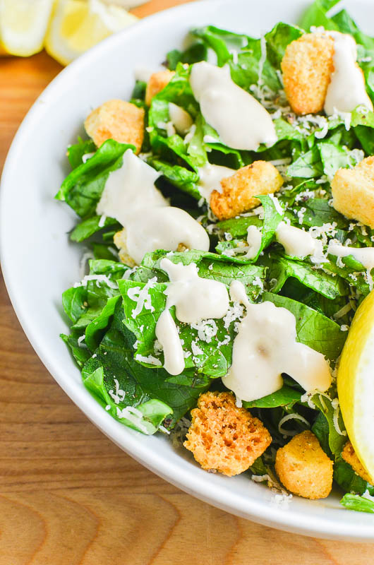 Caesar dressing drizzled over romaine lettuce with croutons, lemons. On a wooden cutting board. 